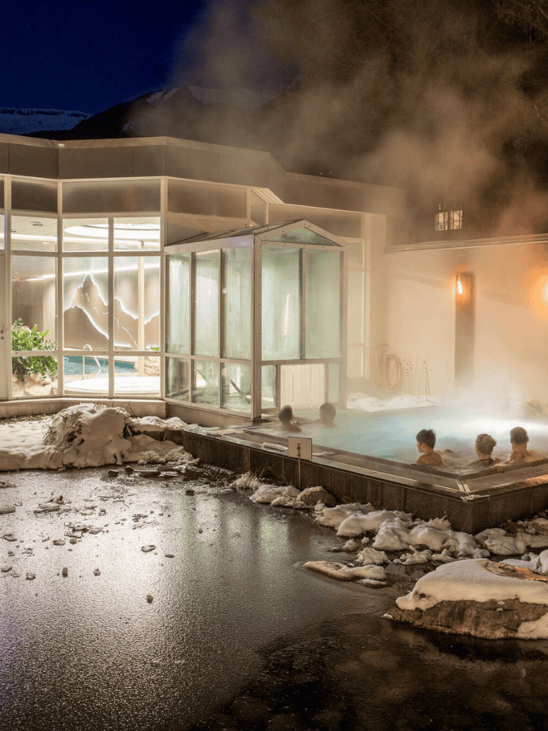 Hot spring spa with steam and snow in winter, outdoor hot tub, relaxing thermal baths, tropical wellness retreat, night setting, cozy atmosphere.