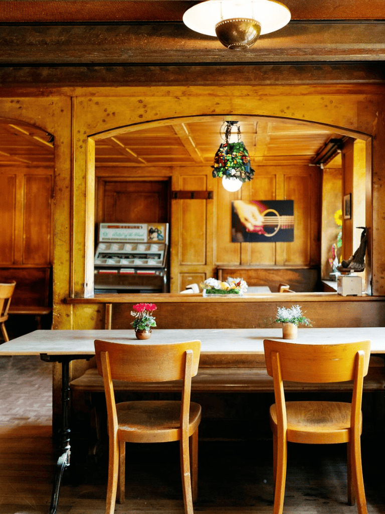 Cozy wooden café interior with table, chairs, and warm lighting, ideal for relaxing and dining.