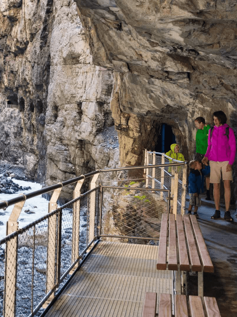 Scenic hiking trail along rocky cliffside featuring families exploring natural tunnel formations.