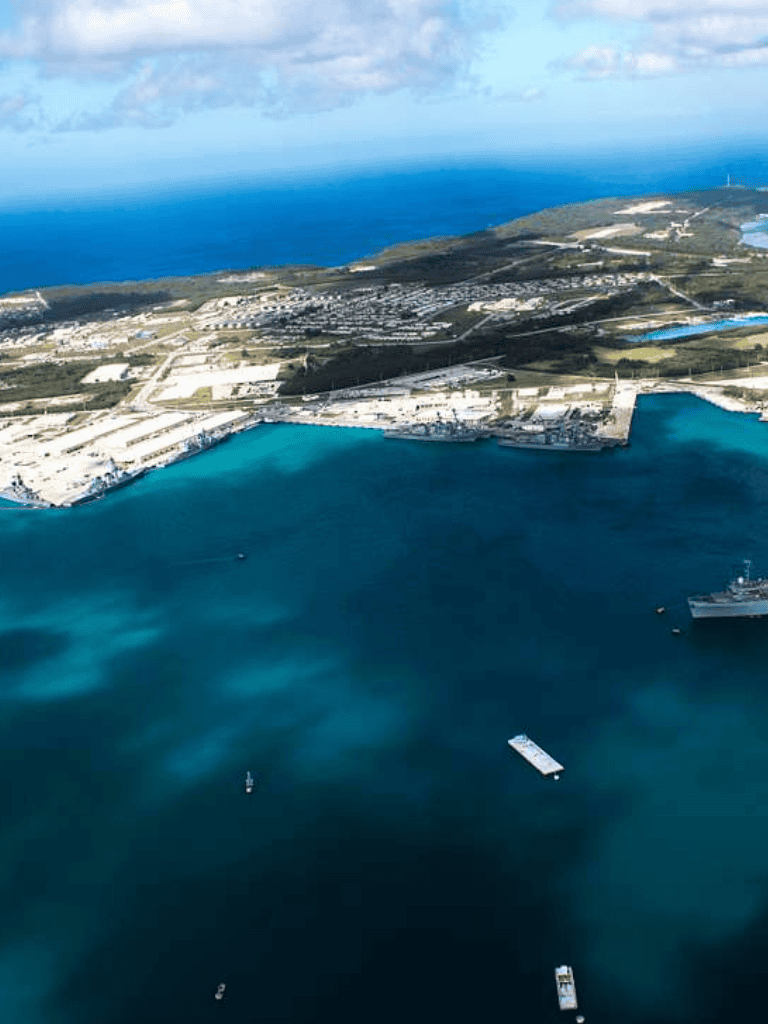 Aerial view of coastal port and industrial area with ships and blue waters in a scenic harbor setting.