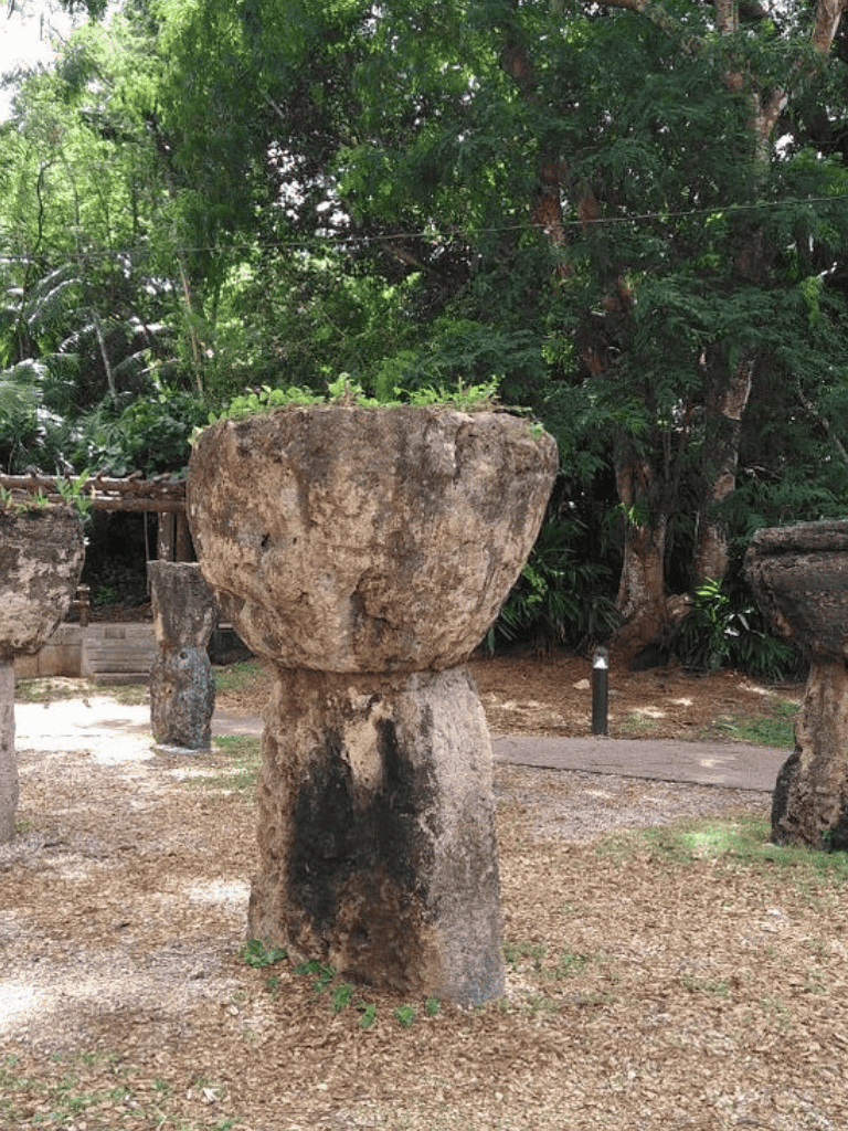 Ancient stone structure resembling a bowl on a pedestal in a lush outdoor setting.