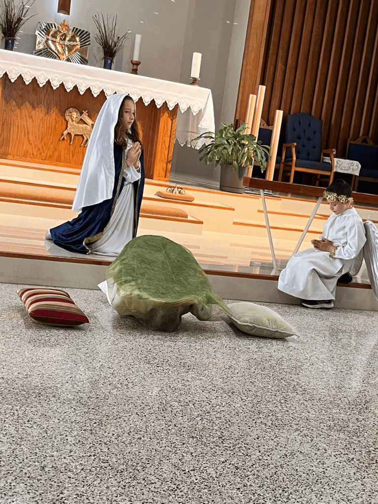 Kneeling girl dressed as Mary and child angel at church nativity scene.