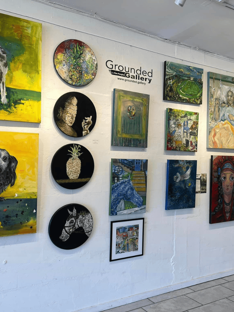 Colorful art gallery display featuring diverse paintings and sculptures at Grounded Gallery.