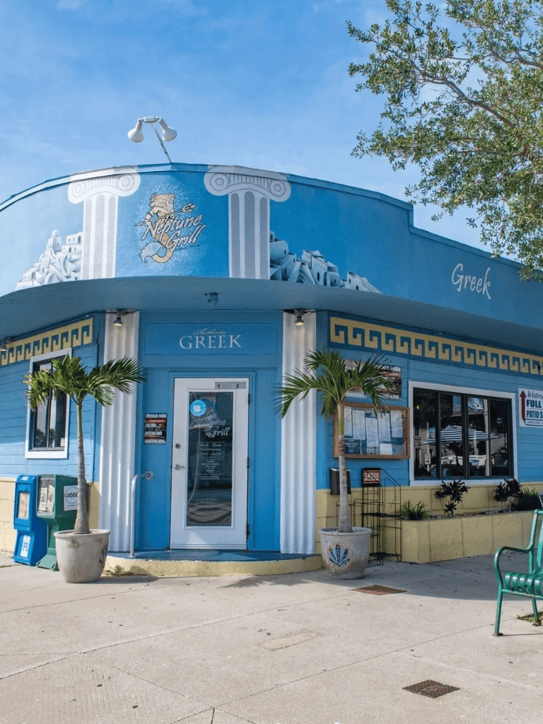 Sunny Greek restaurant with blue exterior and tropical palm trees for a Greek dining experience.