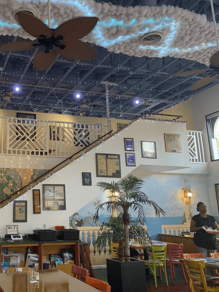 Bright indoor dining area with tropical decor, fairy lights, and ocean-themed murals, perfect for a relaxing dining experience.