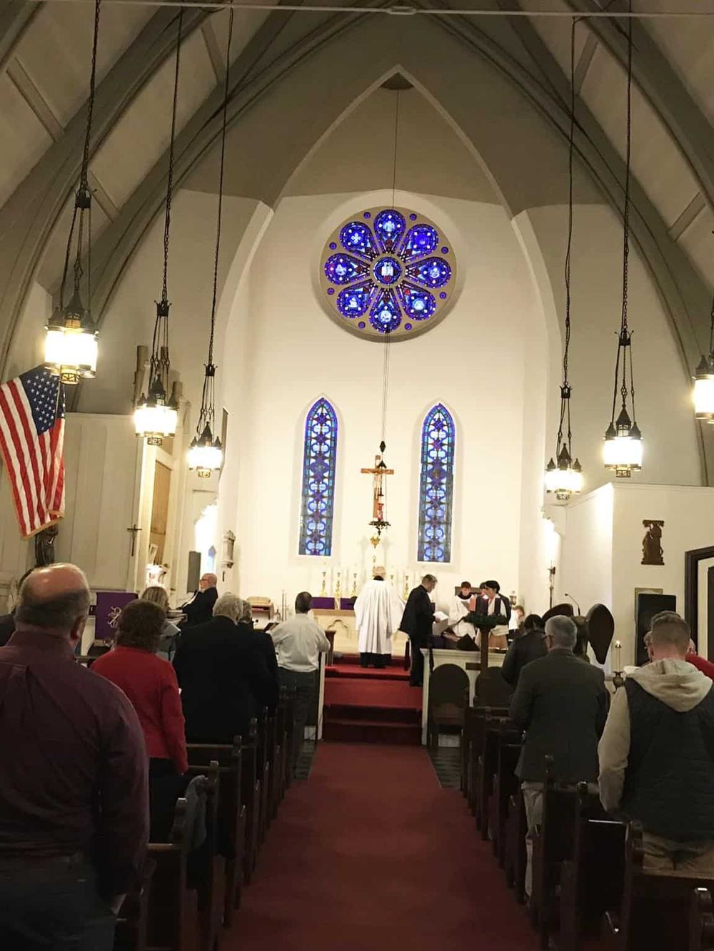 People attending a church service inside a historic sanctuary with stained glass windows and religious symbols.