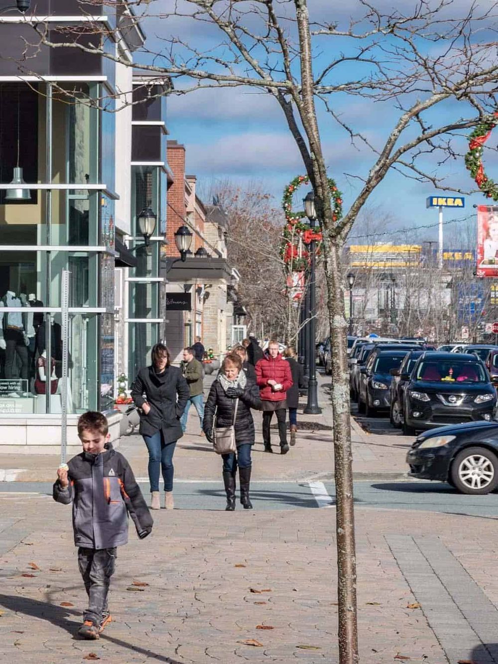 Vibrant city street during holiday season with pedestrians shopping, decorated trees, and retail stores.