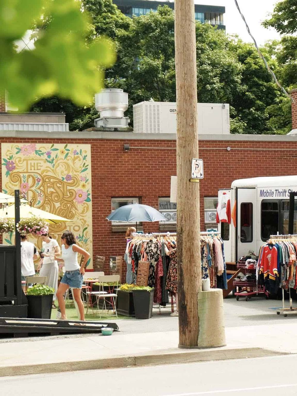 Vintage outdoor street market with clothing racks and shoppers on a sunny day.