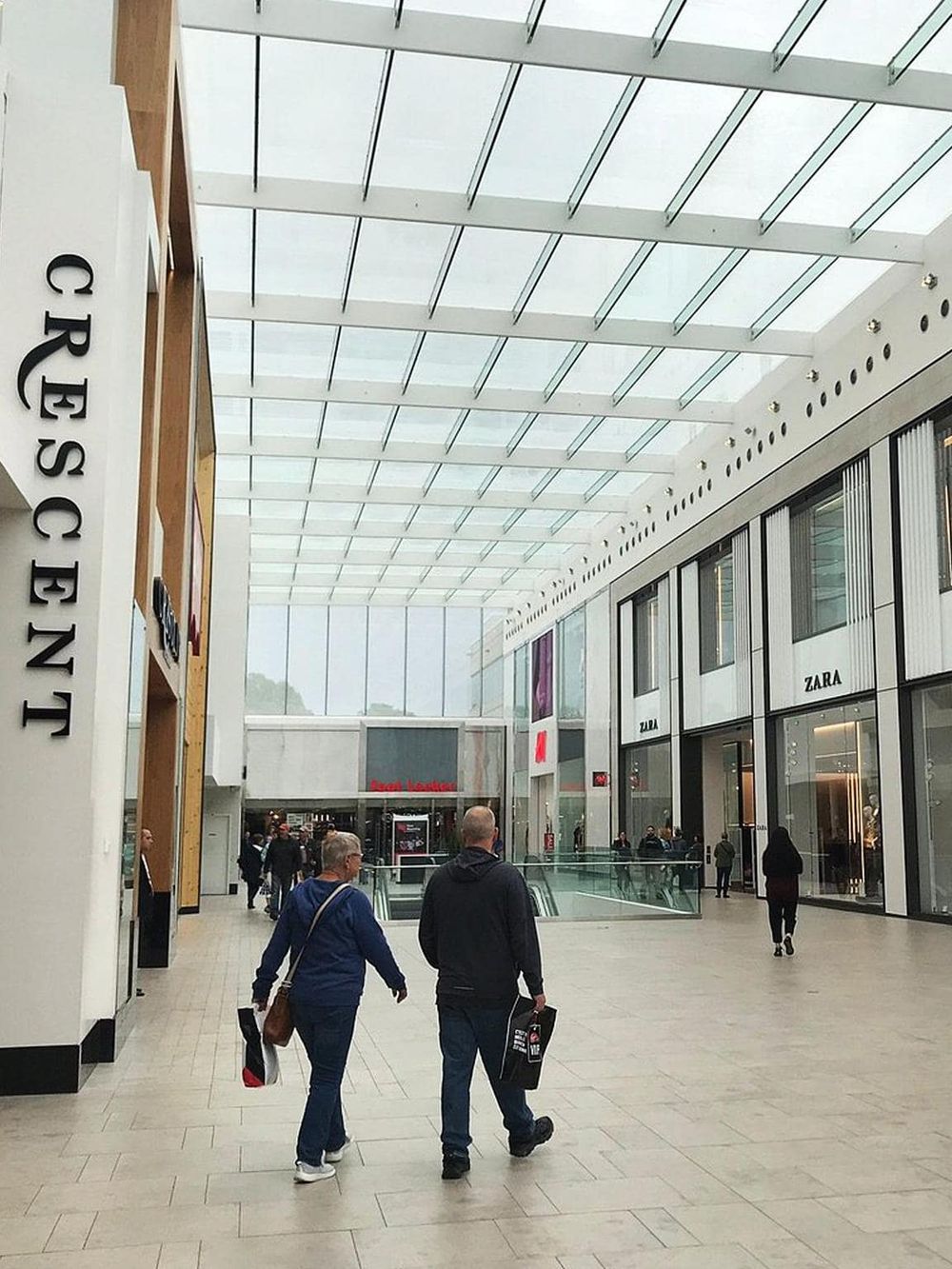 Modern shopping mall interior with high glass ceiling and luxury fashion stores, including Zara and other popular brands.