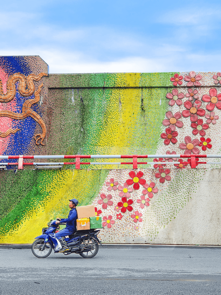 Colorful mural wall with flowers and snake art, motorbike delivery driver in urban street.