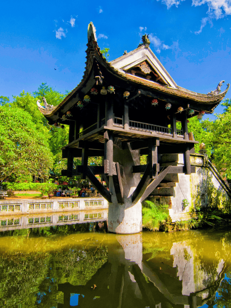 Traditional Thai wooden pavilion on stilts over water, lush green surroundings, clear blue sky.
