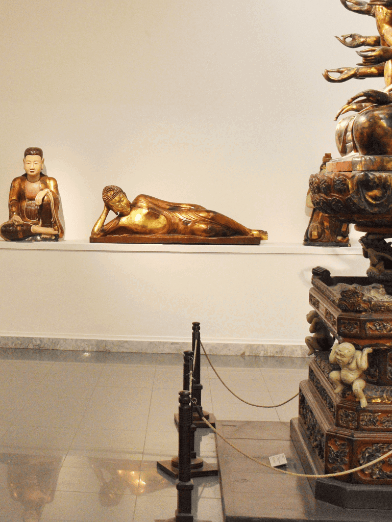 Golden reclining Buddha statue with intricate sculptures in museum.