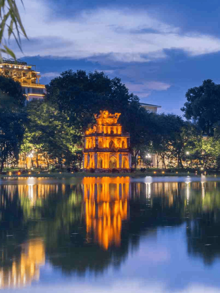 Ancient temple lit up at night reflected in tranquil lake, Vietnam travel destination, scenic evening view.