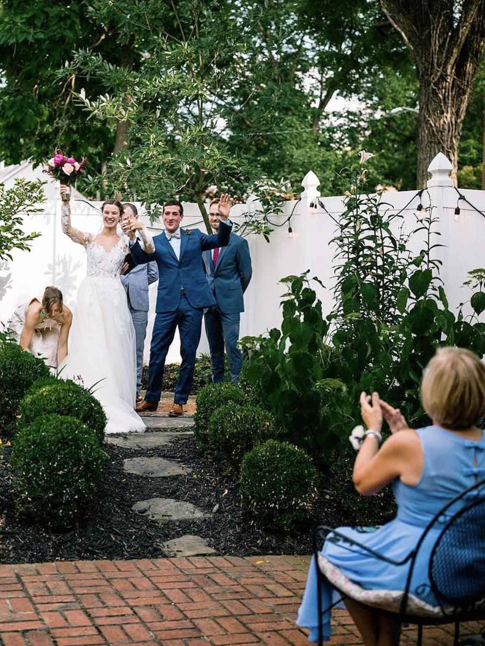 Happy wedding celebration outdoors with bride, groom, and friends in the garden.