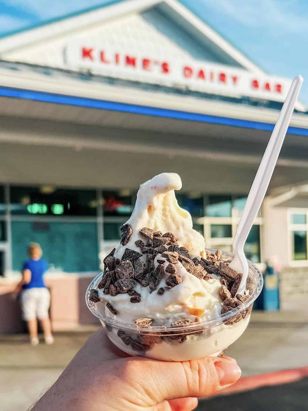 Creamy ice cream sundae with chocolate chunks outside Klien's Dairy Bar, classic American ice cream shop.