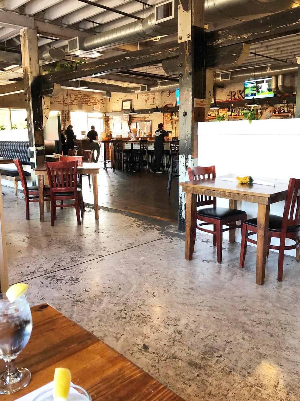 Sunny indoor restaurant with rustic wooden furniture and a lively bar area.