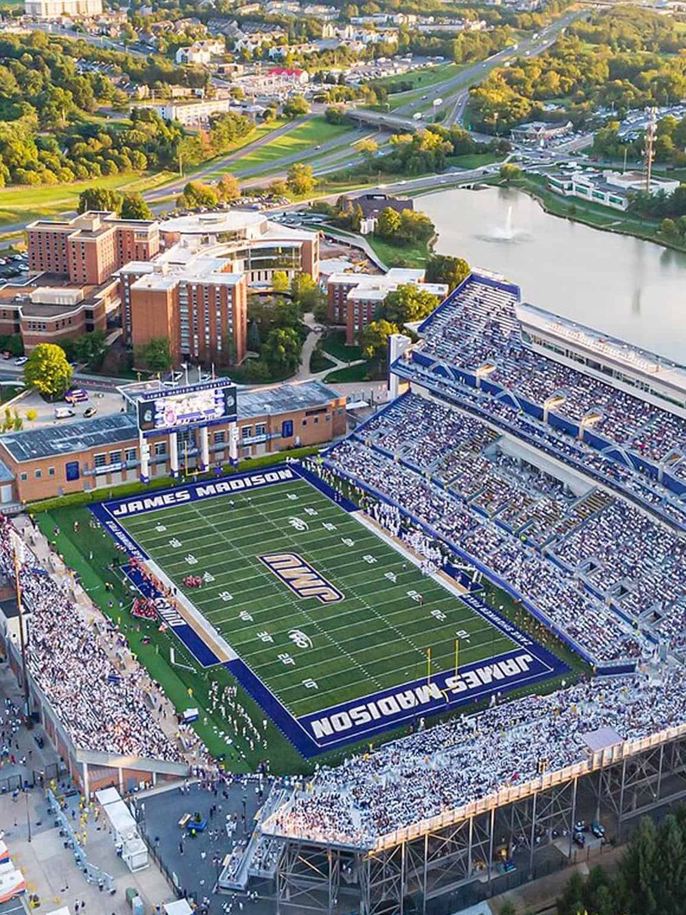 Aerial view of James Madison football stadium and surrounding campus with green landscape and water features.