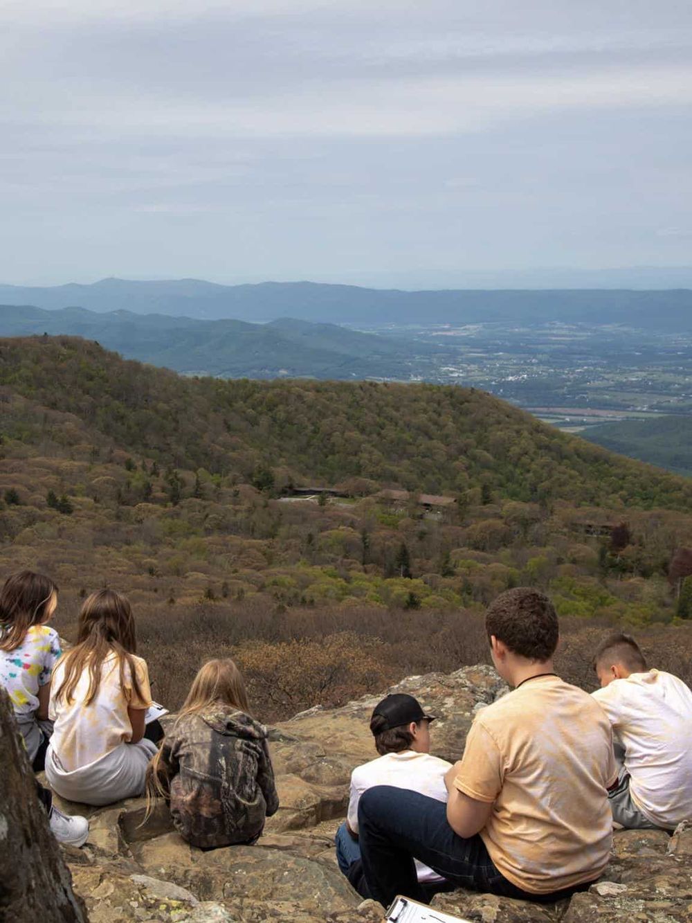 Vast mountain landscape with children sitting on rocks, enjoying outdoor adventure and scenic views for travel inspiration.