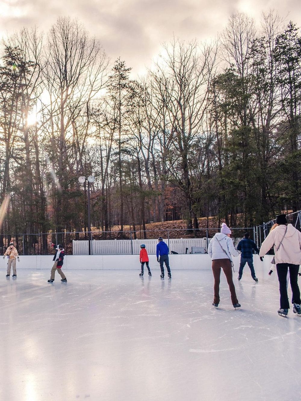 Ice skating at an outdoor rink surrounded by trees, winter weather, and skaters enjoying the cold season.
