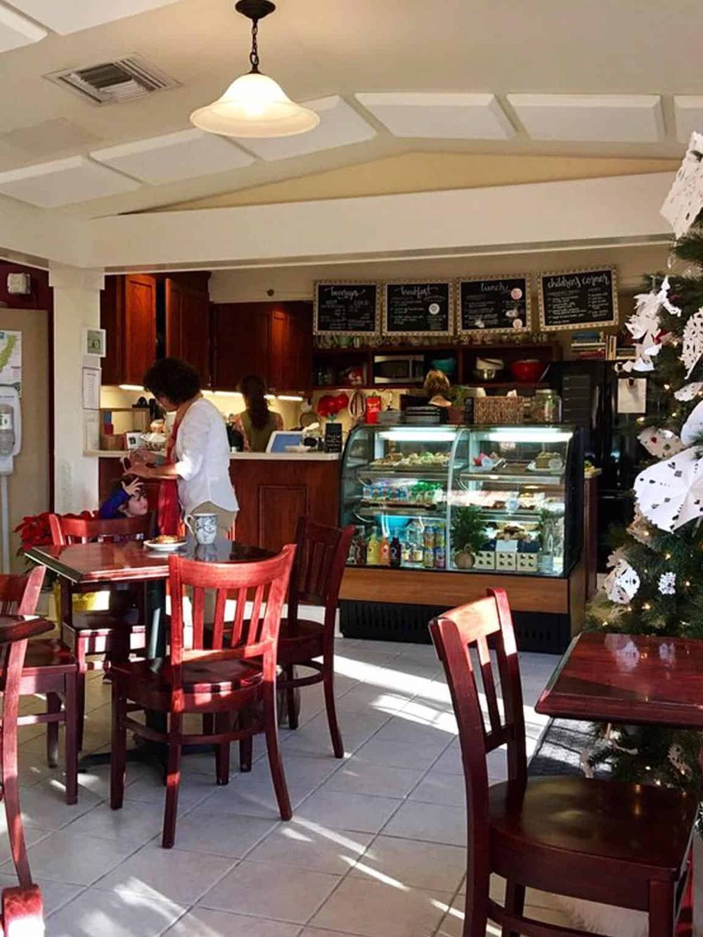 Cozy cafe interior with wooden tables, Christmas decorations, and a display case of desserts and beverages.