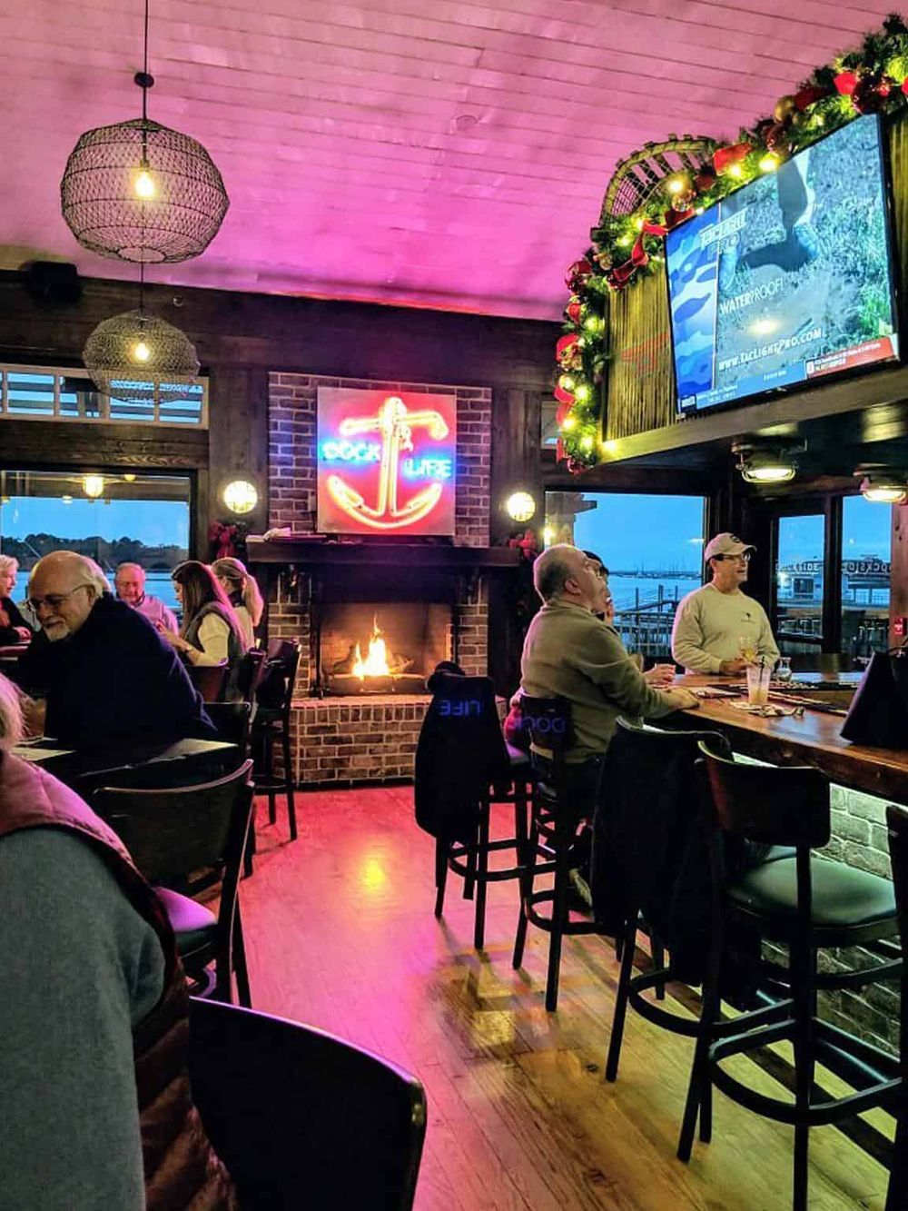 Cozy waterfront restaurant with fireplace, neon sign, and harbor views, ideal for relaxing dining experiences.