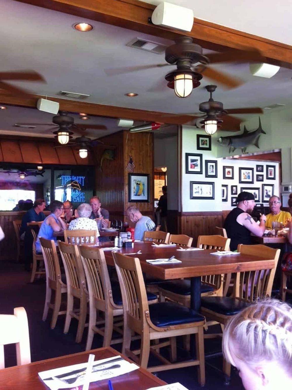 Cozy restaurant interior with wooden accents, ceiling fans, and framed artwork, featuring happy diners enjoying meals.