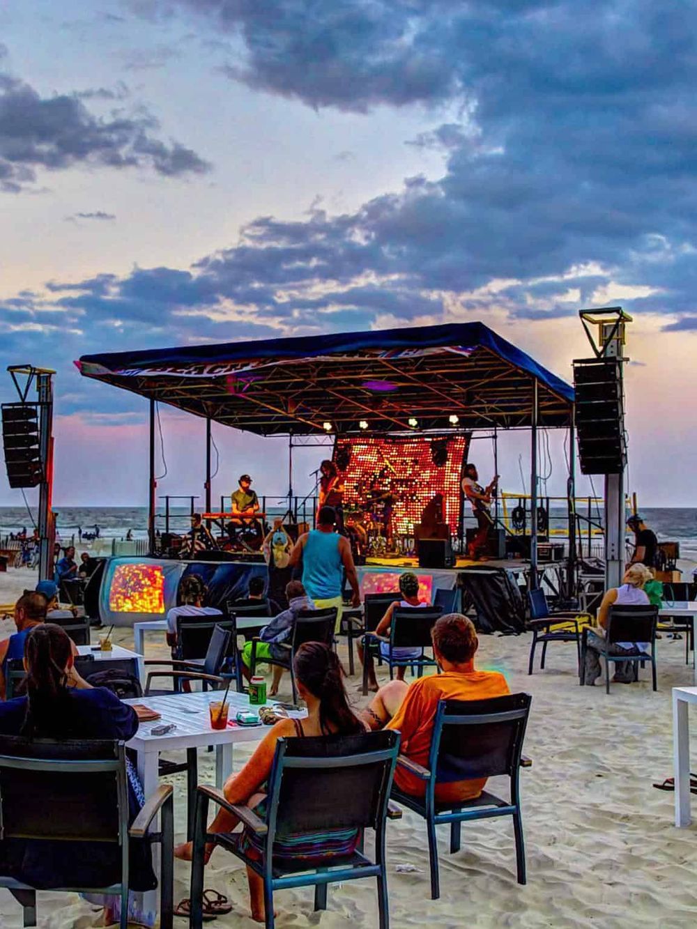 Vibrant beach concert with live band, outdoor seating, and sunset sky, ideal for beach entertainment and relaxation.