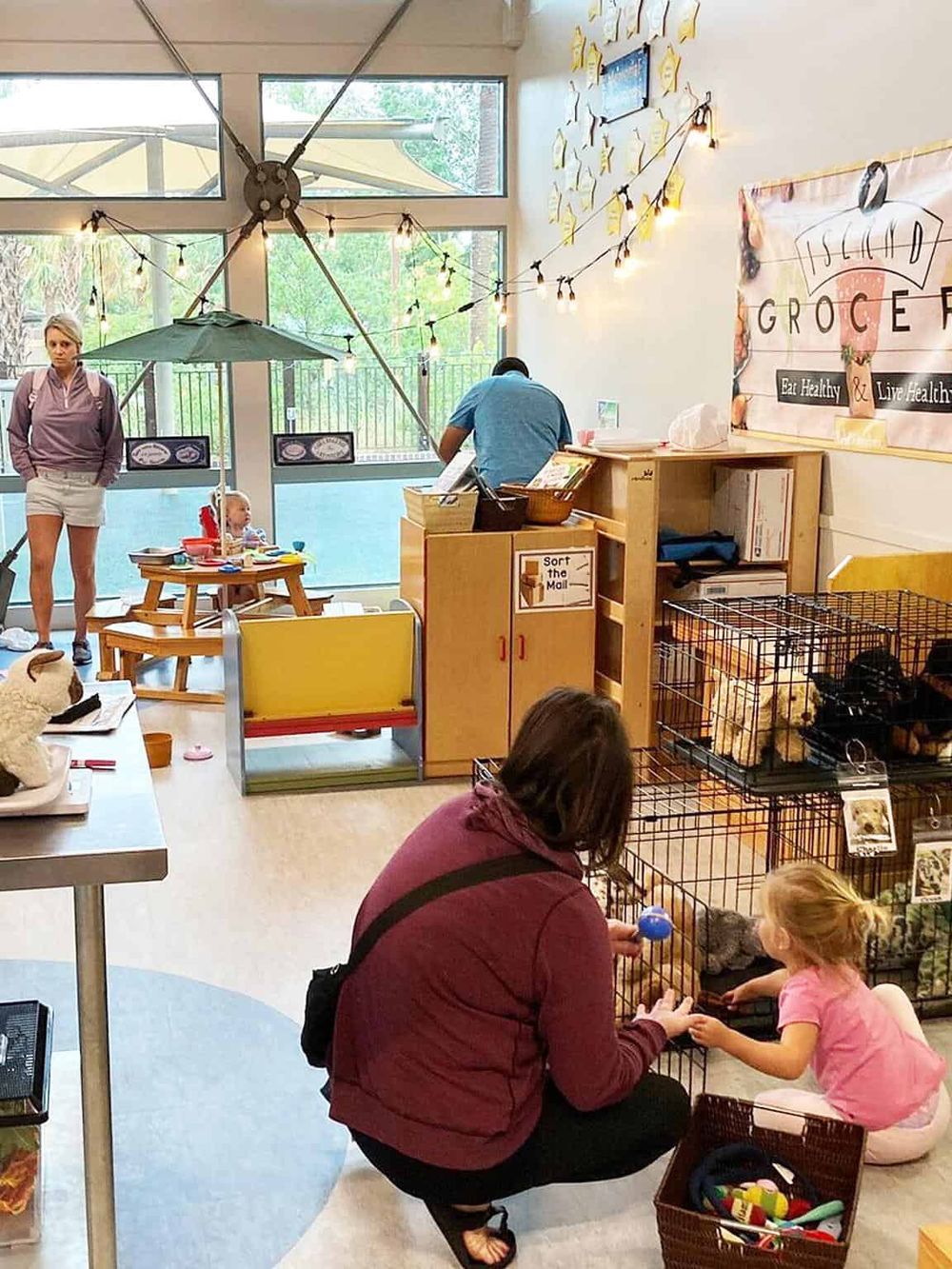Bright indoor pet store with animal cages, a customer interacting with a girl, and a sign promoting healthy living and eating.