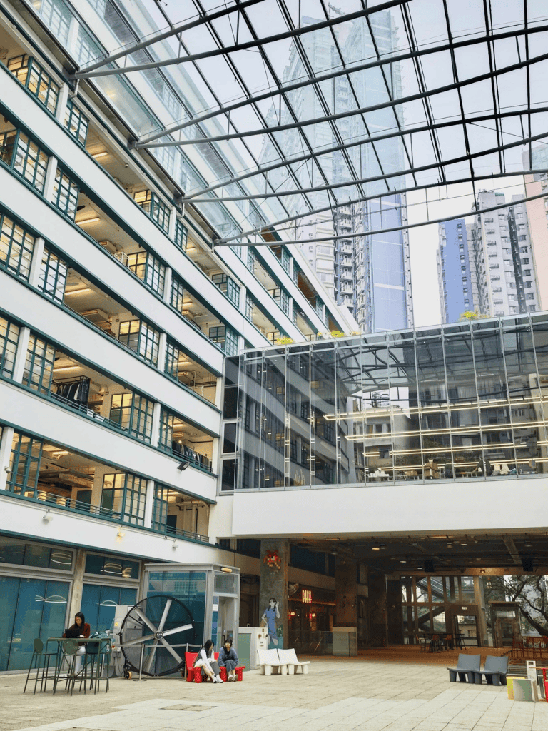 Open-air modern commercial building with glass atrium and seating area, urban cityscape backdrop.