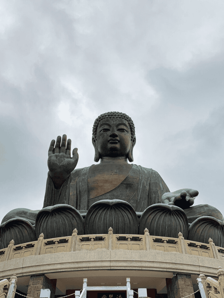 Serene large Buddha statue with raised hand, outdoor setting, cloudy sky, inspiring spiritual monument, peaceful meditation symbol.