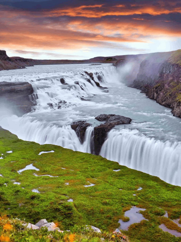 Majestic waterfall cascading over rocks with a vibrant sunset sky in the background.