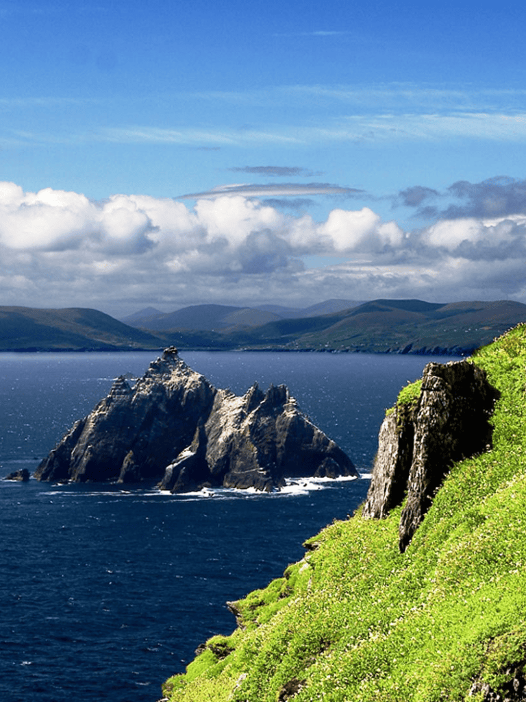 Majestic ocean coast with rocky islands and lush green cliffs under a partly cloudy sky.