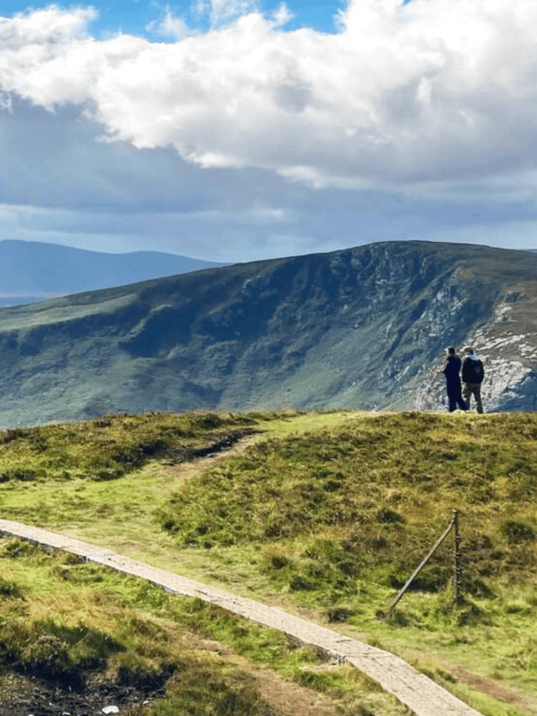 1. Two hikers standing on a mountain trail overlooking lush green hills and distant mountains.