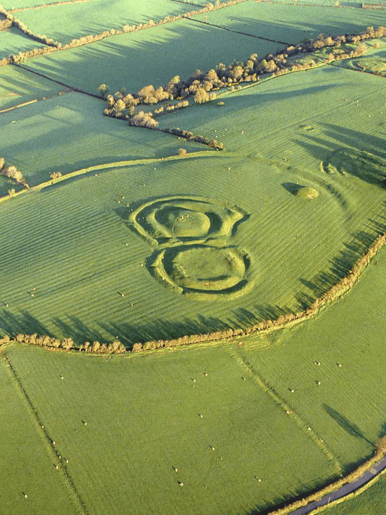 Ancient earthwork spiral formation in green fields, aerial view of prehistoric landscape.