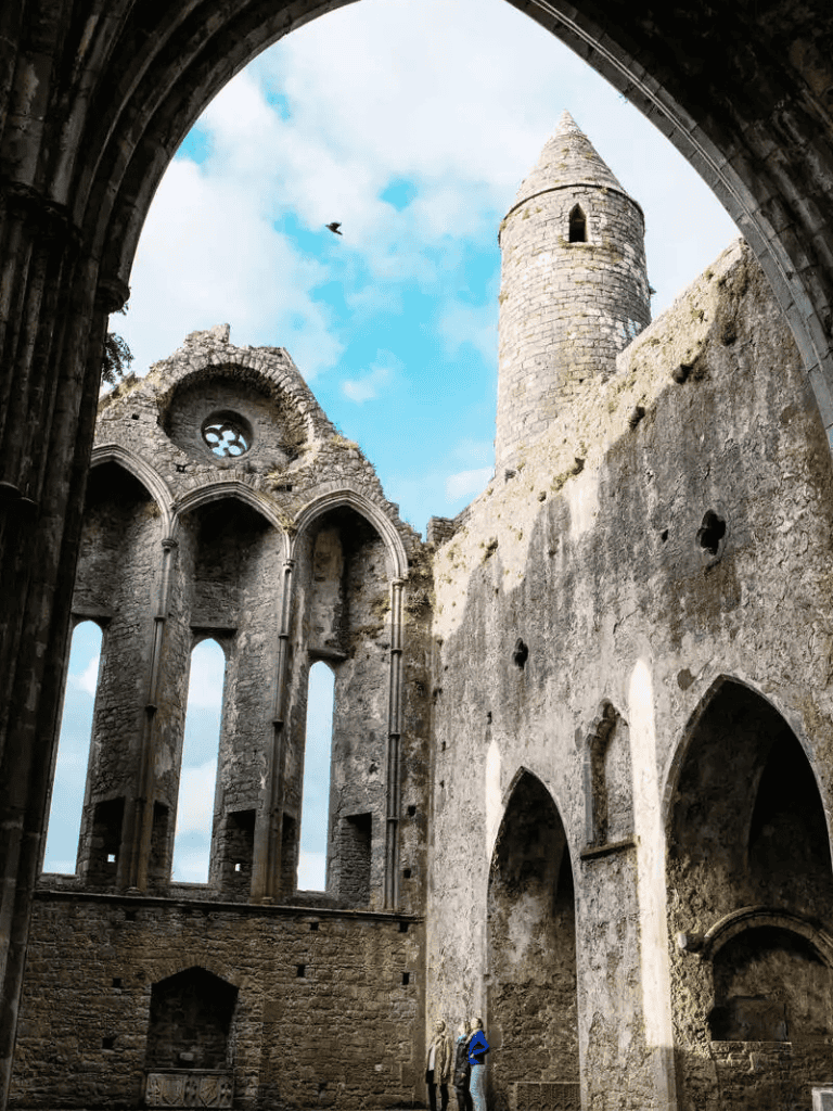 Ancient castle ruins with towering stone walls and a turret under a blue sky.