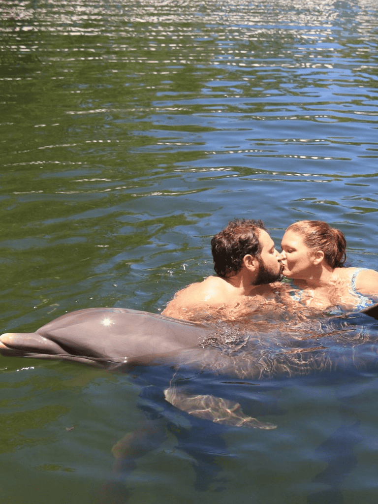 Loving couple kissing with dolphin in natural water setting, romantic water adventure, QuestForDirections.