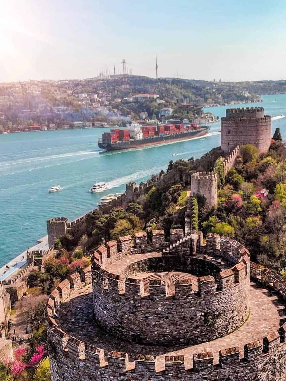 Large cargo ship sailing through Bosphorus Strait with historic Rumeli Fortress in Istanbul, Turkey.