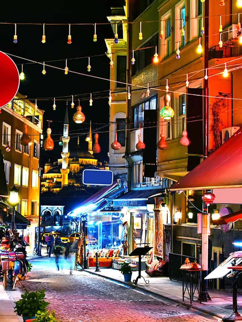 Colorful night street scene with vibrant lights, shops, and pedestrians in a lively urban area.