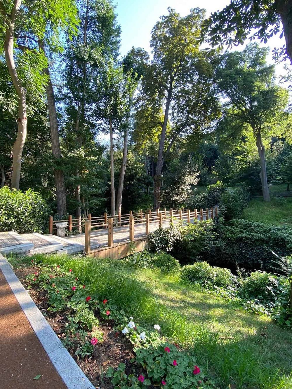 Peaceful garden with pathway and wooden railing in a lush green park setting.
