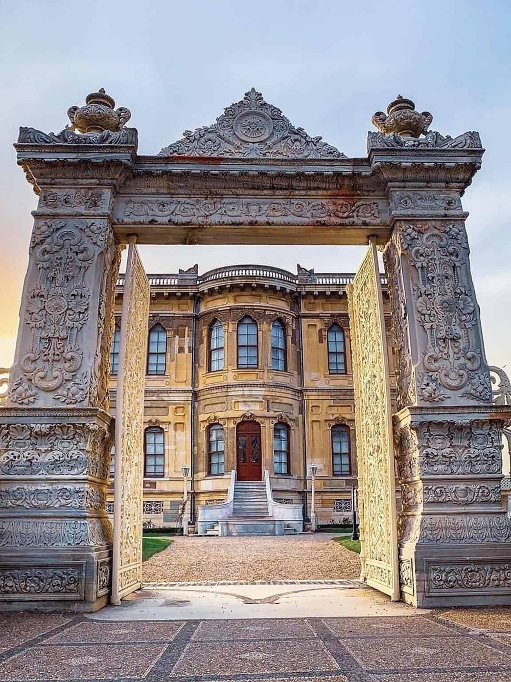Intricate stone gate leading to a grand historic mansion or palace, showcasing architectural elegance and detailed craftsmanship.