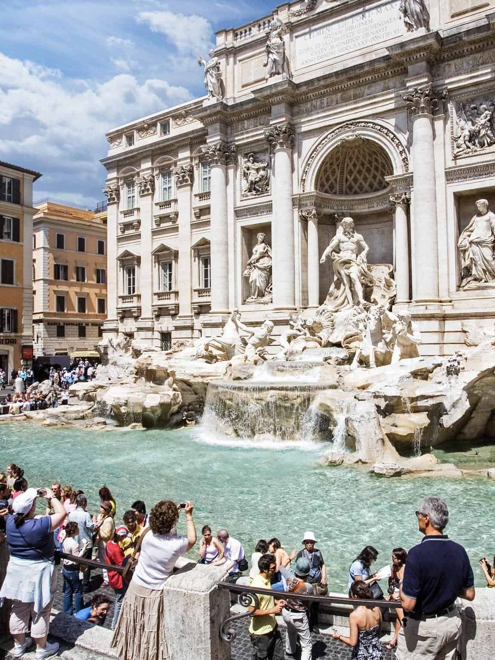 Majestic Trevi Fountain in Rome, Italy with tourists capturing photos, iconic baroque architecture, and historic scenery.