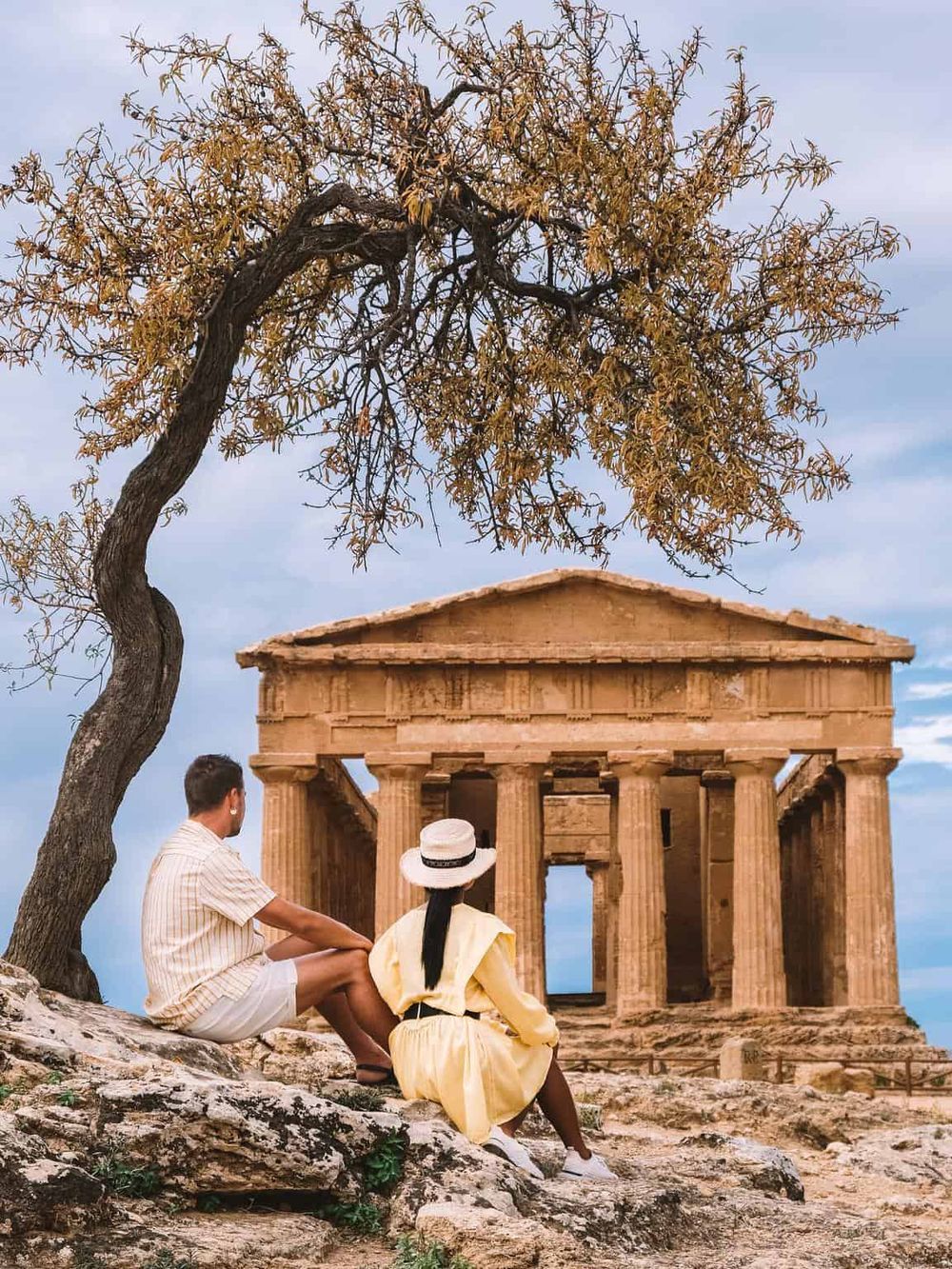 Ancient Greek temple ruins with visitors and a large tree, emphasizing historical exploration and sightseeing.