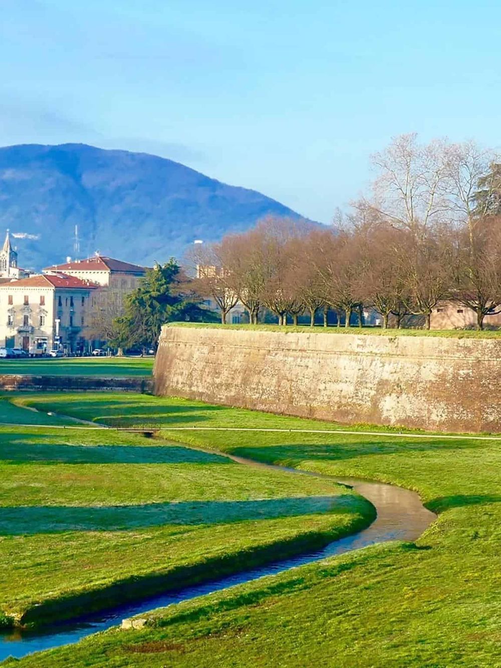 Historic city park with lush greenery, scenic streams, and mountain views, perfect for walking and relaxation.