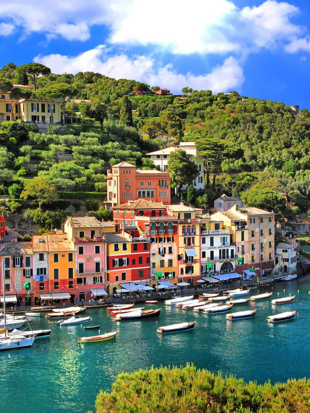 Colorful Mediterranean harbor with vibrant buildings and boats in clear water, scenic hillside seaside destination.
