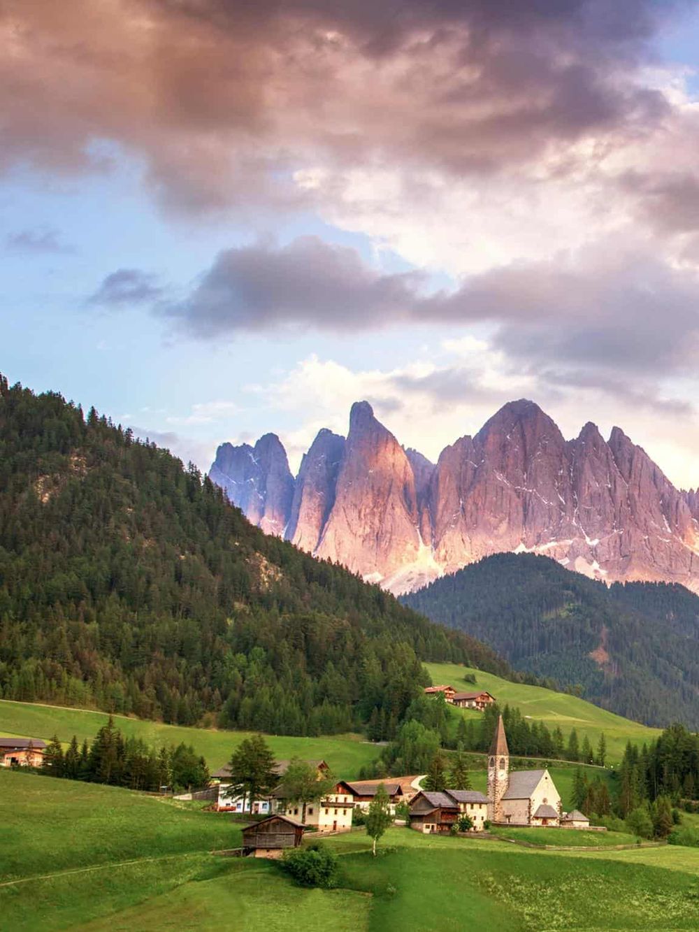 Vibrant mountain village surrounded by lush green hills and striking peaks in the Italian Alps.