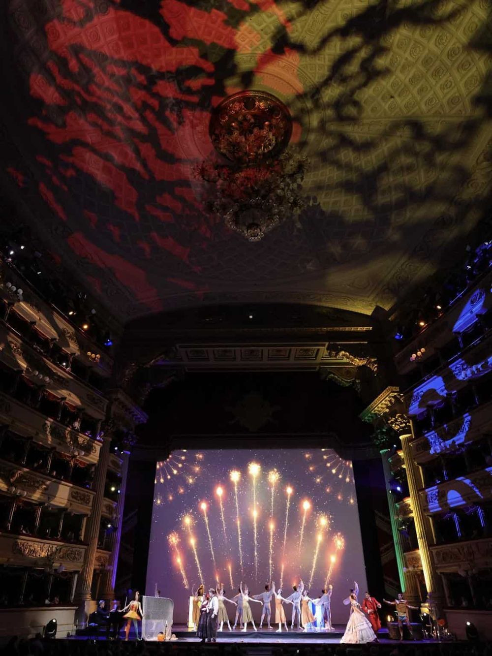 Colorful theater stage with dancers, fireworks projection, and ornate interior, showcasing QuestForDirections event planning expertise.