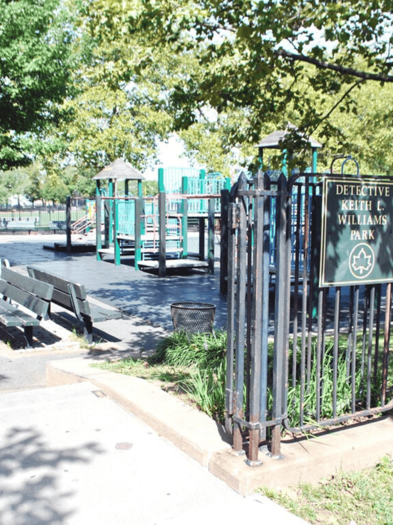 Playground at Detective Keith L. Williams Park in McKinney, TX, with benches, trees, and safety fencing.