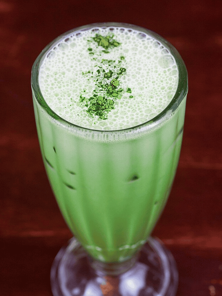 Fresh Green Matcha Latte in Tall Glass with Frothy Top and Green Garnish.