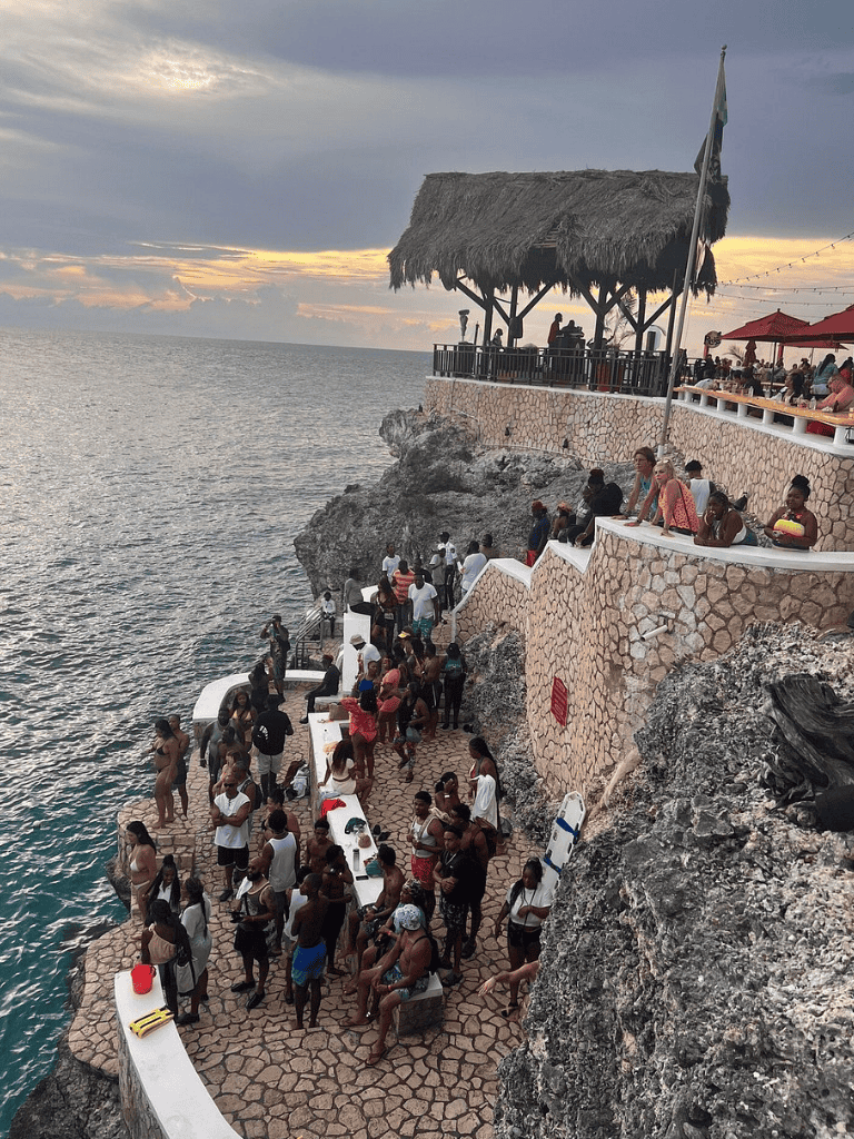 Cliffside ocean view at QuestForDirections seaside restaurant with thatched roof and sunset sky.