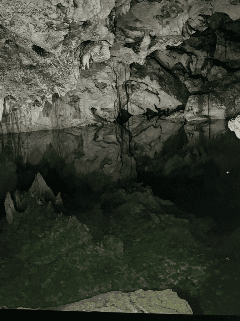 Ice cave interior with stalactites and stalagmites, reflected in a still water pool.